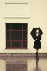 Young fashion woman in black coat with umbrella walking in city street