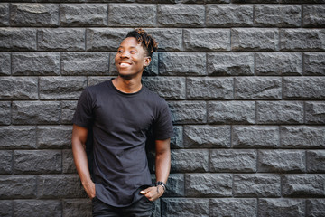 Handsome african american man in blank black t-shirt standing against brick wall