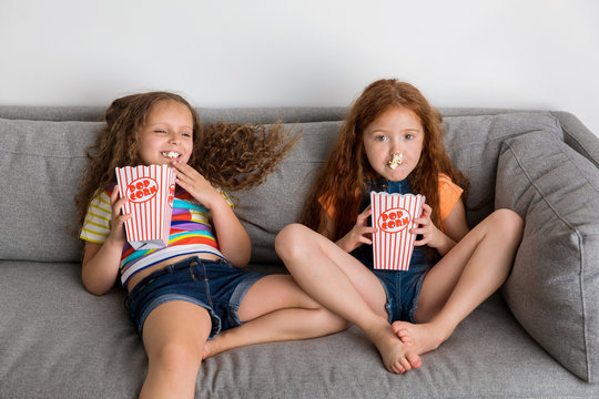 Young girls on grey sofa eating pop corn