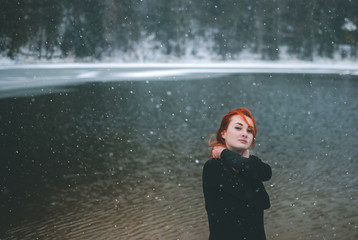 Snowflakes flying over handsome black-eyed redhead girl looking at the camera and playing with her beautiful hair. Closeup of falling snowflakes
