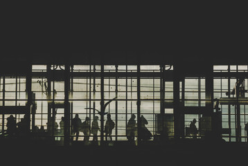 Black sillhouettes of people huttying up to take a train on a subway station behind glass windows filled with sunshine. Berlin, Germany
