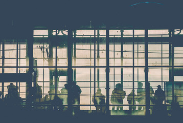 Black sillhouettes of people waiting for their train on a subway station behind glass windows...