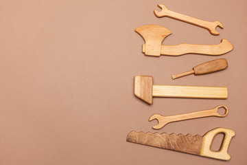 view from above on a wooden hand-made set with tools for the child. A wooden hammer, a saw, a wrench, a screwdriver, an ax are toys for a boy. beige background with place for text
