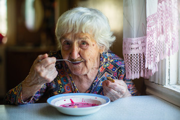 An elderly woman eating soup borsch sitting at the table.
