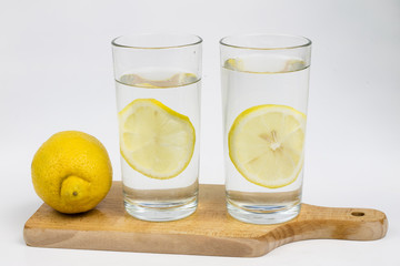 A glass of cold water with lemon on a white kitchen table. A refreshing drink in warm weather.