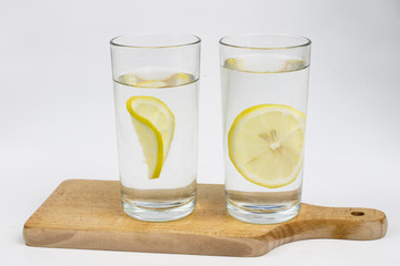 A glass of cold water with lemon on a white kitchen table. A refreshing drink in warm weather.