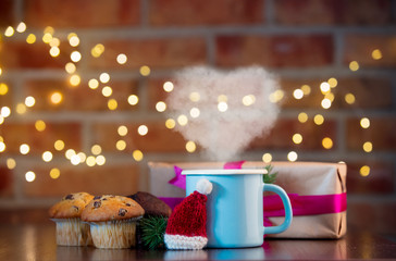 Homemade classic and chocolate cupcakes and cup with heart shape steam. Fairy lights in bokeh. Christmas time concept