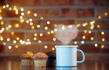 Homemade classic and chocolate cupcakes and cup of tea with heart shape steam. Fairy lights in bokeh.