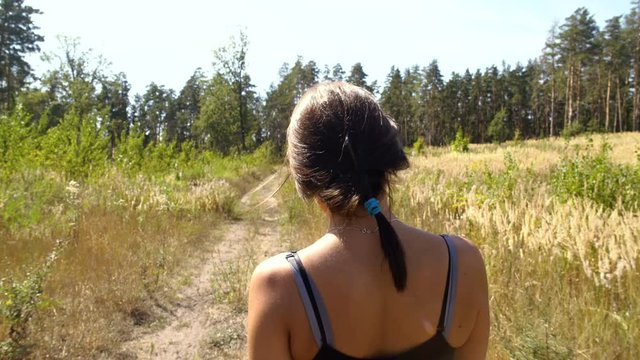 A girl walks along a forest trail, a sports caress, a back view