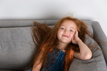 smiling redhead little girl resting on grey couch