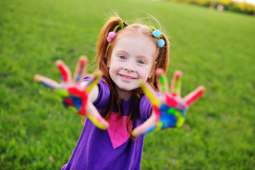 red-haired girl preschooler shows palms stained with multicolored finger paints