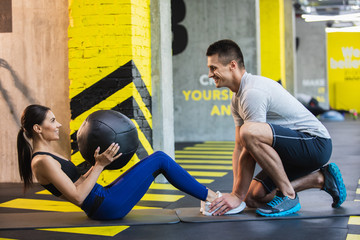 Cheerful lady is doing abs crunches while lifting medical ball. Her male partner is feeling happy...
