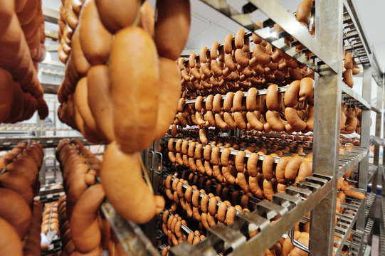 Sausages hanging in a smoking chamber close-up against a meat-packing plant