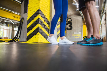 Low angle of male and female legs in gym. They are wearing sneakers and sport clothes while spending active time together. Copy space in left side