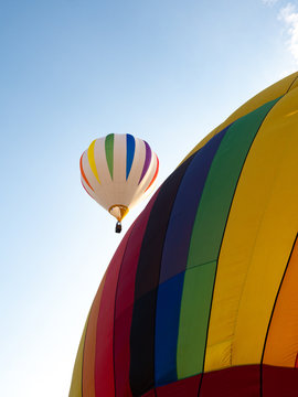 Close Up of a Stationery Hot Air Balloon with a white balloon with colorful accents in Flight in the Background