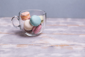 Multicolored macaroons in a glass cup on a gray-blue background. Copy spase.