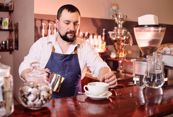 portrait of a handsome bearded barista preparing coffee on the background of a coffee shop and a coffee machine