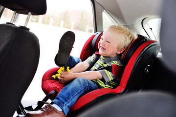 portrait of a young child of a boy with blond hair in a children's car seat. Safe transportation of...