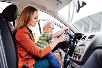 a young mother with a small child sits behind the wheel of a car. Family trip