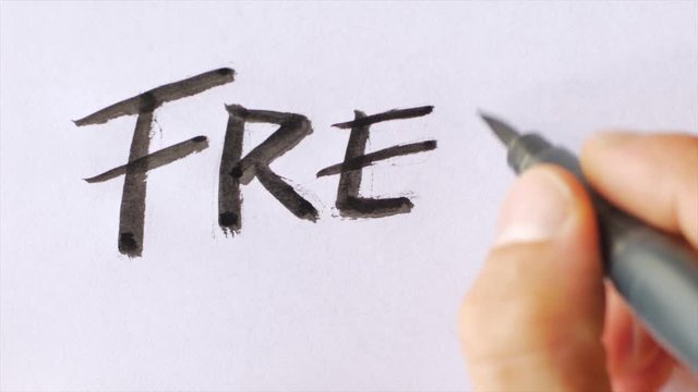 Hand writing the word FREE in capital block letters on white paper