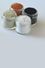 Top view of kaolin powder, activated charcoal, red, green and green cosmetic clays in jars. Deep cleansing bentonite (montmorillonite) clay for beauty spa face mask, body detox and hair treatments. 