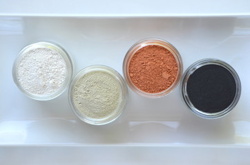 Top view of kaolin powder, activated charcoal, red, green and green cosmetic clays in jars. Deep cleansing bentonite (montmorillonite) clay for beauty spa face mask, body detox and hair treatments. 