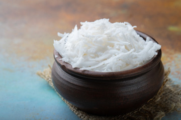 Coconut flakes in a clay bowl on a blue background