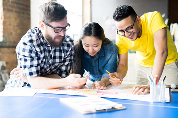 Naklejka premium Portrait of three creative young business people making up plan chart while standing at desk in modern office