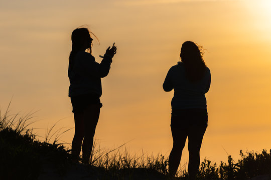 Two women silhouetted  by the setting sun on a sand dune in Assateague Island.