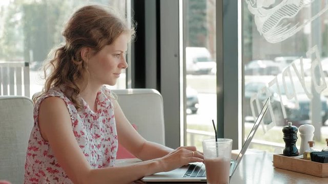 Young business woman sits at a table at a restaurant. She carried a laptop with access to the Internet, it checks the mail . She looks very happy