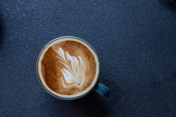 Top view of a cup of hot latte with white foam, placed on the rough table background