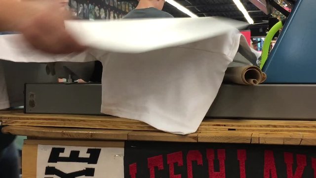T shirt business steams on design to clothing before pulling it from heating machine.