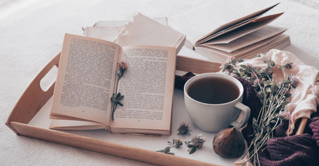 Composition of a cup of tea and opened book is not readable on a coffee table in the room, with figs and flowers. close up