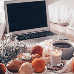 Breakfast in bed, a tray of tea, croissants, fruit, flowers and laptop Morning. Blogger theme. concept of working at home