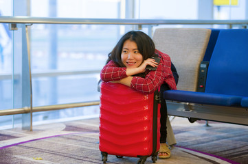 happy and pretty Asian Chinese tourist woman sitting at airport departure boarding gate with suitcase hand luggage waiting for flight on in holidays travel