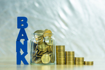 BANK text with Coin money in the glass jar on table, for saving and banking finance concept.