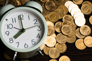 Alarm clock and coins stacks on working table in dark room, time for savings money concept, banking and business concept.