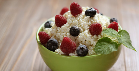 Cottage cheese in green bowl with raspberries and blueberries on wooden background. Healthy Breakfast.