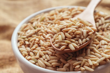 Raw brown rice in a spoon and bowl. top view food background
