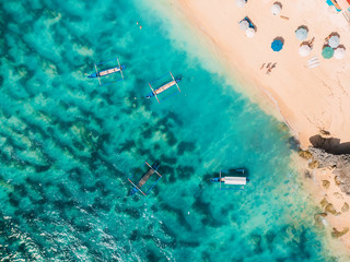 Aerial view of sandy beach with turquoise sea water and local boats, drone shot