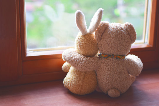 Best friends teddy bear and bunny toy sitting on brown window sill hugging each other and looking out of window on vintage tone. Love, family and friendship background.