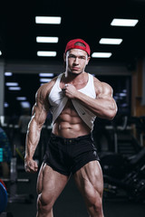 Naklejka na ściany i meble Muscular athletic bodybuilder fitness model posing and exercises in gym