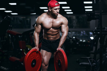 Muscular athletic bodybuilder fitness model posing and exercises in gym