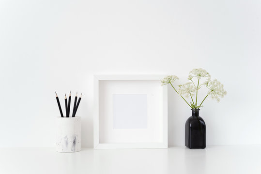 Modern white square frame mockup with a Aegopodium in black vase and black pencils on white background. . Template for small businesses, lifestyle bloggers, social media