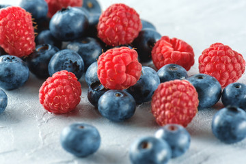 Blueberries and raspberries on the background of gray cement. Ripe and juicy fresh raspberries and blueberries close-up. A lot of berries close-up.