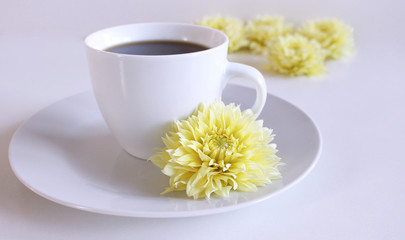 A cup of black coffee and yellow dahlia flower on the table.