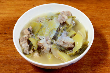 Pickled lettuce soup with spare rips and streaky pork in white blow on wooden table. Thai traditional local northern food.