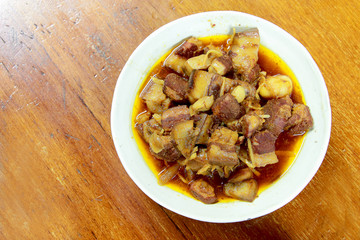 Northern Thailand local dish called Gaaeng Hang Laeh Moo is a Northern Style Hang Lay Curry with Thai herb, streaky pork, pickled onions in a bowl on wooden table. Thai traditional local northern food