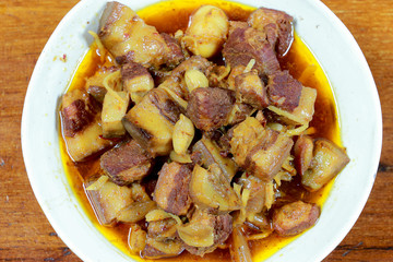 Northern Thailand local dish called Gaaeng Hang Laeh Moo is a Northern Style Hang Lay Curry with Thai herb, streaky pork, pickled onions in a bowl on wooden table. Thai traditional local northern food