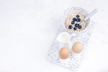 Boiled eggs for breakfast, oatmeal porridge and milk in white dishes on a light background. Delicious and healthy breakfast. Free space for text. Top view. Copy space.